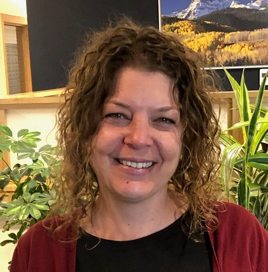 Friendly woman smiling in Lakewood with plants and mountain landscape in background.